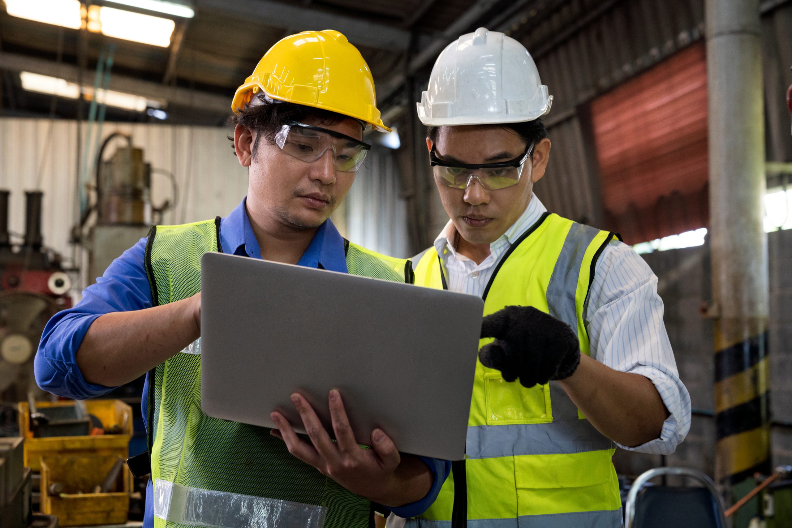 Manufacturing worker. Confident male workers with laptop at manufacturing plant. Concentrated workers showing control machine on laptop to technician.